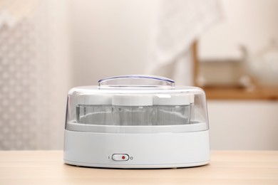 Photo of Modern yogurt maker with empty jars on table indoors