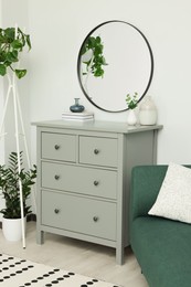 Photo of Chest of drawers and stylish round mirror on white wall indoors. Interior design