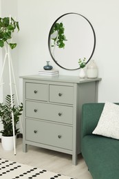 Chest of drawers and stylish round mirror on white wall indoors. Interior design