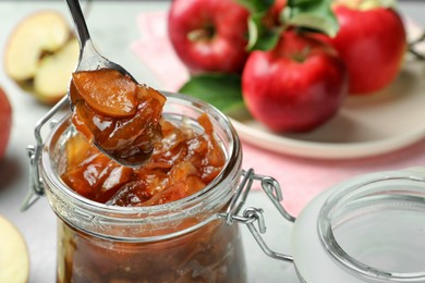 Photo of Spoon with tasty apple jam over glass jar at table, closeup. Space for text