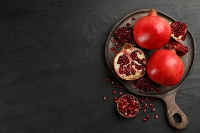 Photo of Delicious ripe pomegranates on black table, flat lay. Space for text