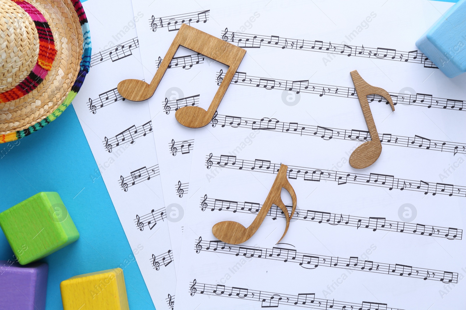 Photo of Baby songs. Music sheets, wooden notes, cubes and hat on light blue background, flat lay