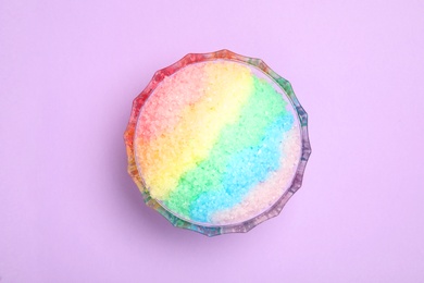 Photo of Rainbow shaving ice in glass dessert bowl on lilac background, top view