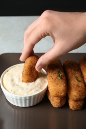 Photo of Woman dipping cheese stick into sauce at table, closeup