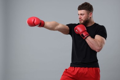 Photo of Man in boxing gloves fighting on grey background. Space for text