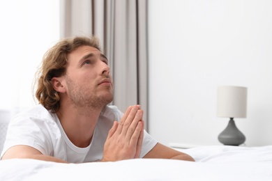 Handsome young man saying bedtime prayer at home. Space for text