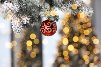 Photo of Beautiful red holiday bauble hanging on Christmas tree against blurred fairy lights, closeup