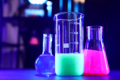 Photo of Glassware with luminous liquids on table in laboratory