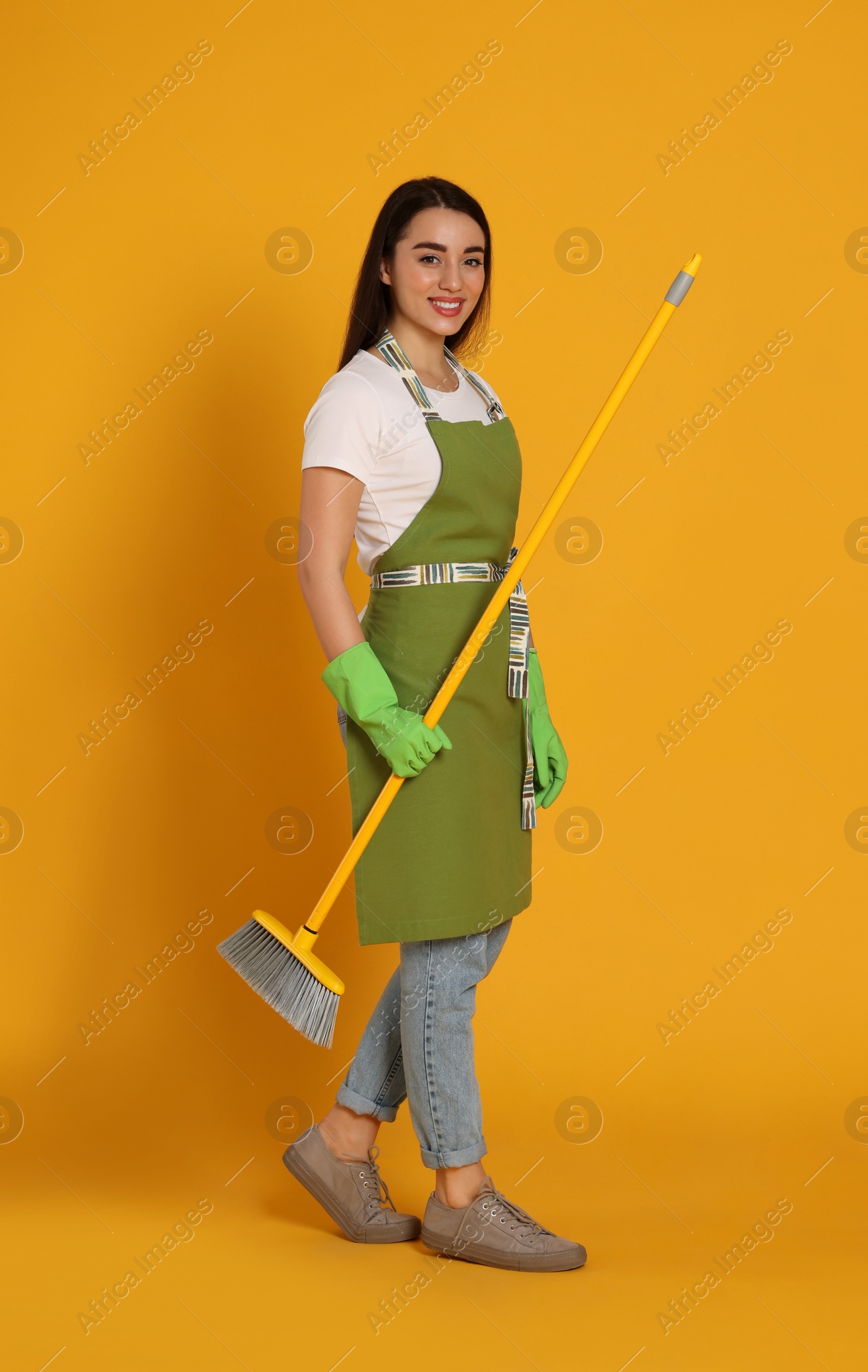 Photo of Beautiful young woman with broom on yellow background