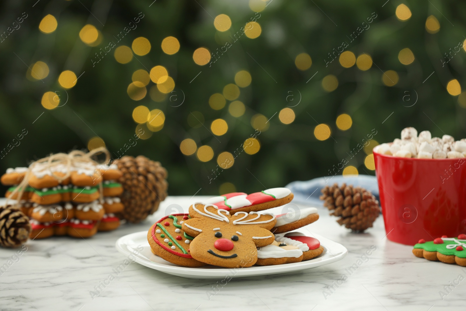 Photo of Decorated cookies and hot drink on white marble table against blurred Christmas lights