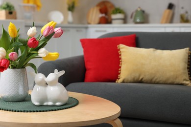 Photo of Easter decorations. Bouquet of tulips and bunny figures on table near sofa indoors. Space for text
