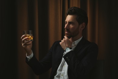 Man in suit holding glass of whiskey with ice cubes on brown background