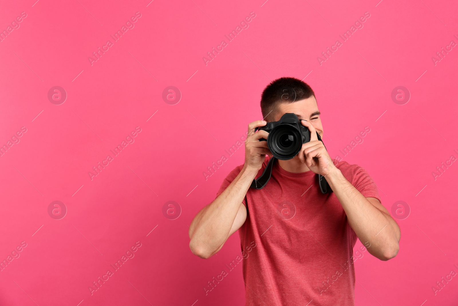 Photo of Young professional photographer taking picture on pink background. Space for text