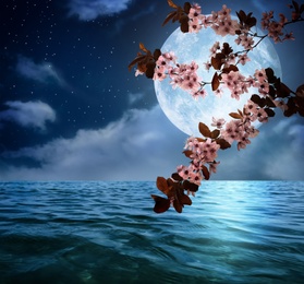 Image of Fantasy world. Blossoming cherry tree branch and full moon in starry sky over ocean