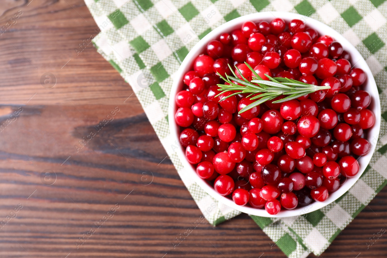 Photo of Fresh ripe cranberries in bowl on wooden table, top view. Space for text