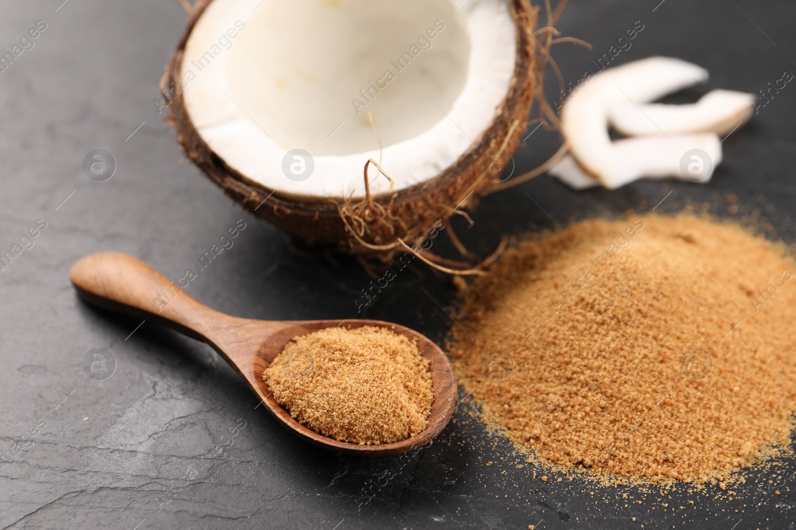 Photo of Coconut sugar, spoon and fruit on dark textured table, closeup