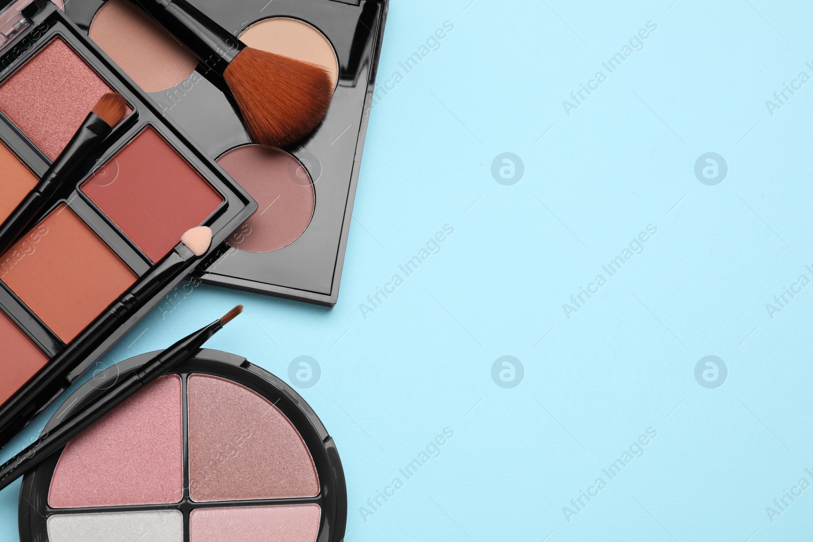 Photo of Colorful contouring palettes and brushes on light blue background, flat lay with space for text. Professional cosmetic product