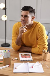 Photo of Man with sketchbook and felt tip pen at wooden table indoors