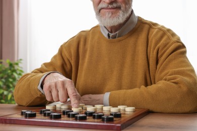Photo of Playing checkers. Senior man thinking about next move at table in room, closeup