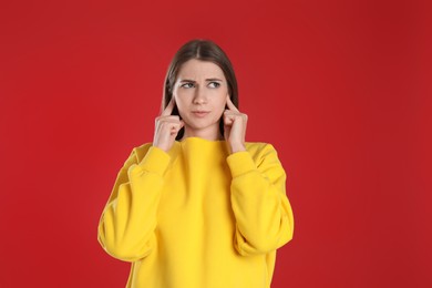 Photo of Emotional young woman covering her ears with fingers on red background