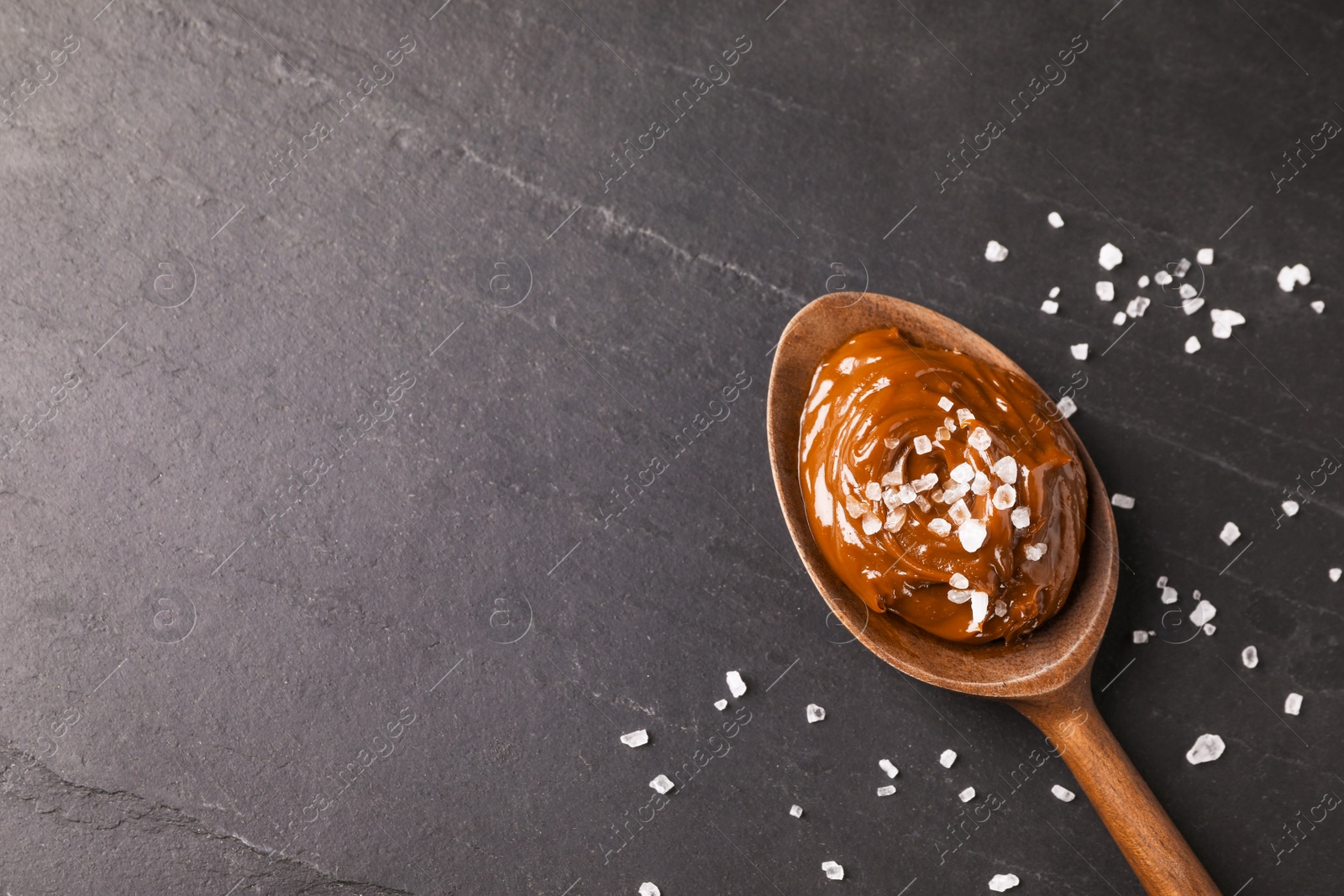 Photo of Salted caramel in spoon on grey table, flat lay. Space for text