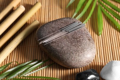 Photo of Stone with acupuncture needles on bamboo mat, above view