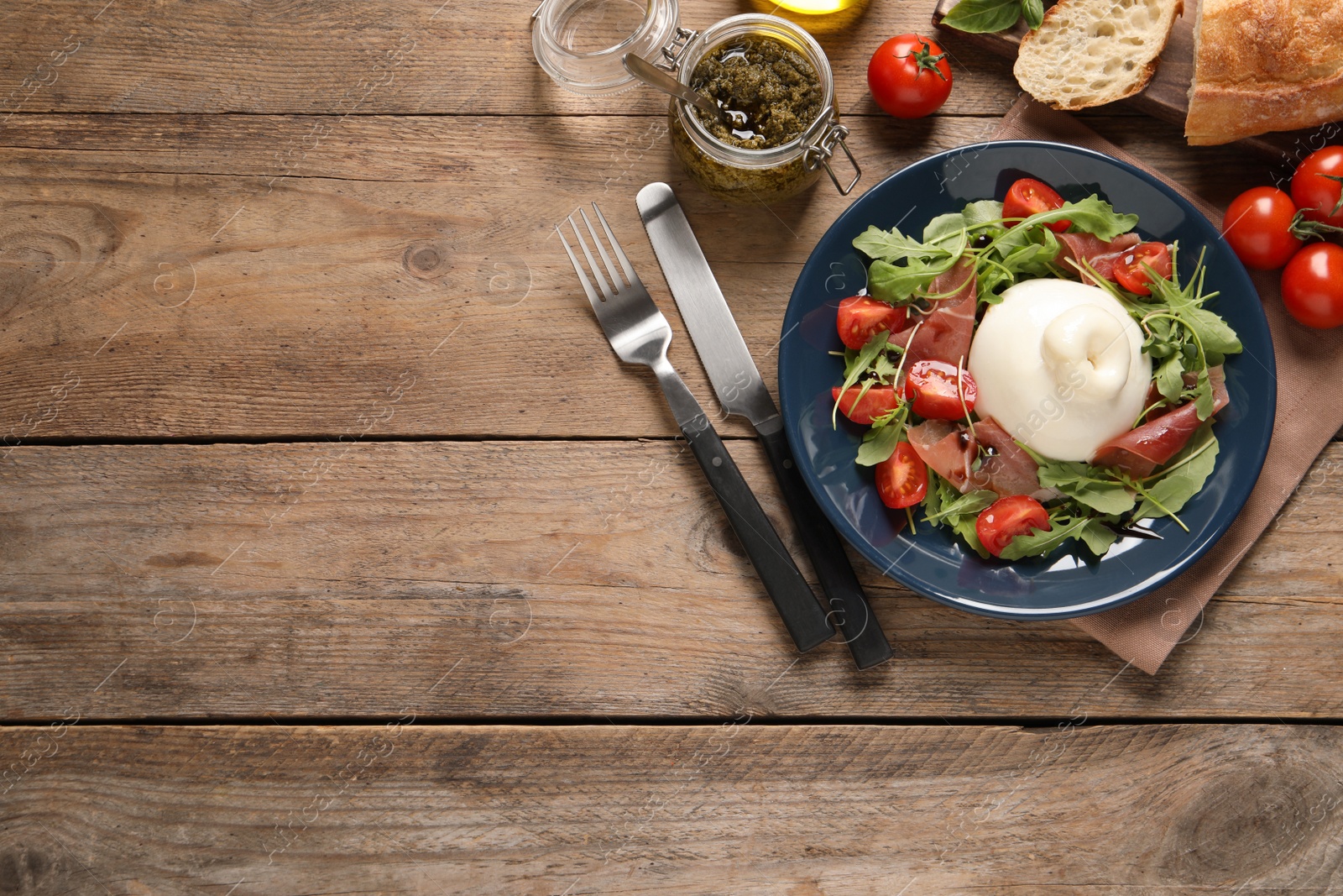 Photo of Delicious burrata salad with tomatoes, prosciutto and arugula served on wooden table, flat lay. Space for text