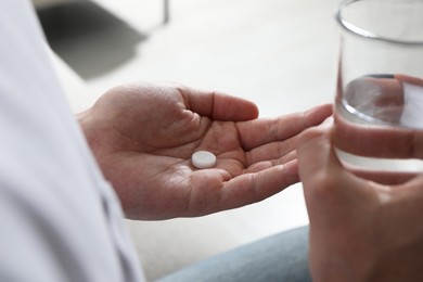 Photo of Man with glass of water and pill on blurred background, closeup