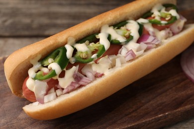 Photo of Delicious hot dog with onion, chili pepper and sauce on table, closeup