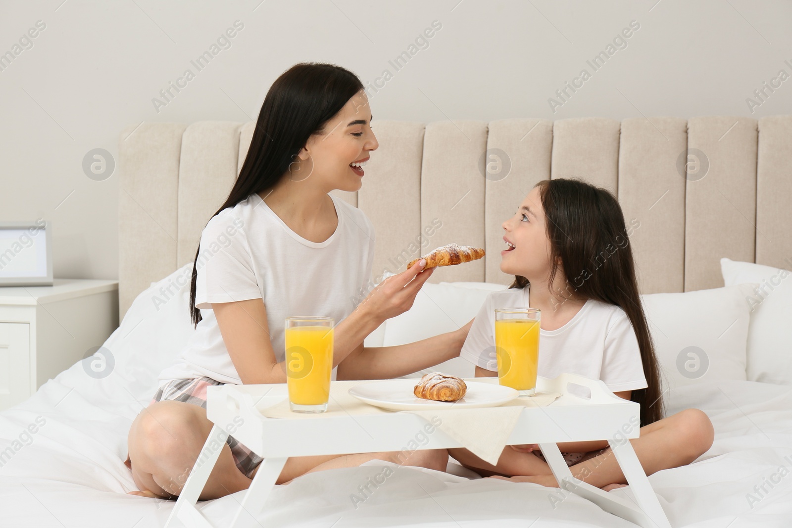 Photo of Young mother and her daughter having breakfast on bed at home