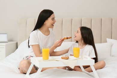 Photo of Young mother and her daughter having breakfast on bed at home
