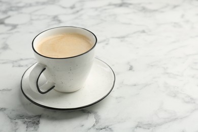 Photo of Tasty cappuccino in cup and saucer on white marble table, closeup. Space for text