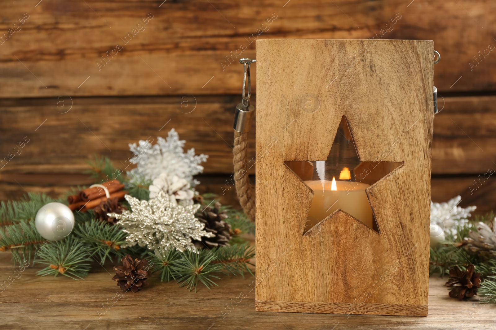 Photo of Christmas lantern with burning candle and festive decor on wooden table. Space for text