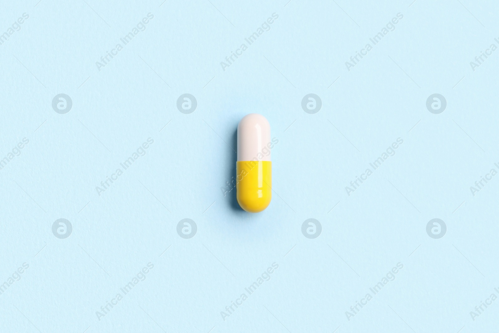 Photo of One pill on light blue background, top view