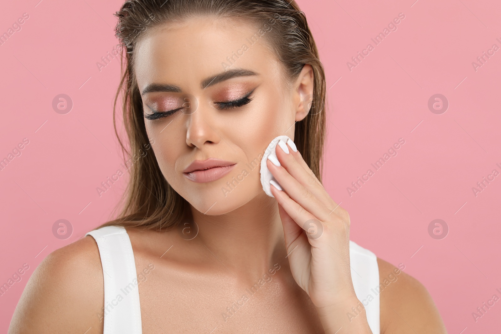 Photo of Beautiful woman removing makeup with cotton pad on pink background