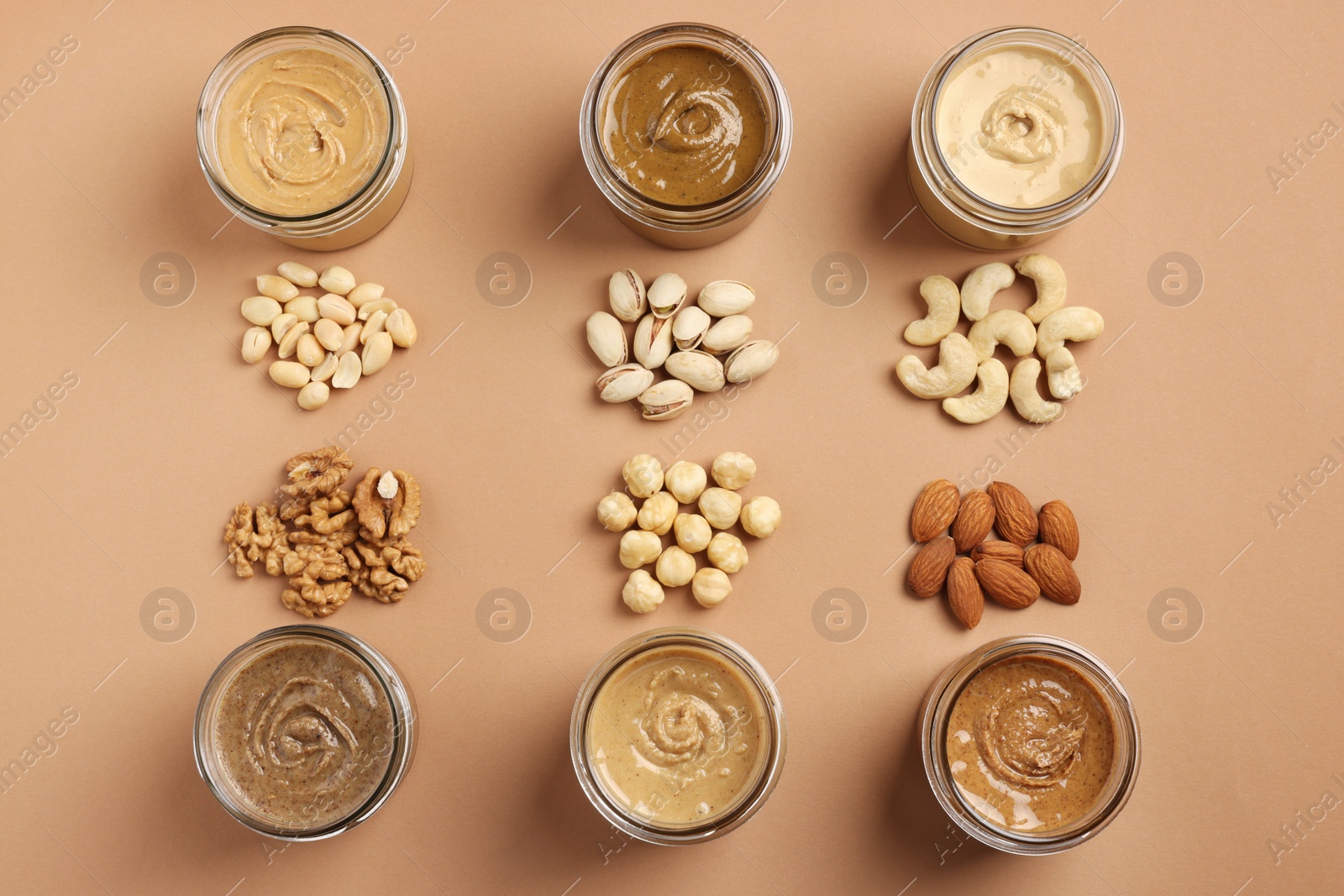 Photo of Many tasty nut butters in jars and nuts on beige table, flat lay