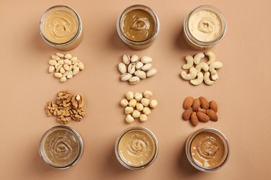 Many tasty nut butters in jars and nuts on beige table, flat lay