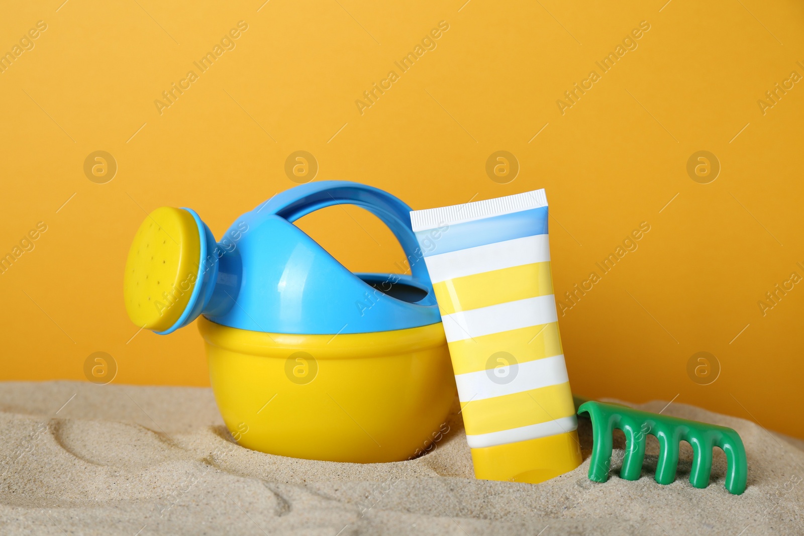 Photo of Suntan product and plastic beach toys on sand against yellow background