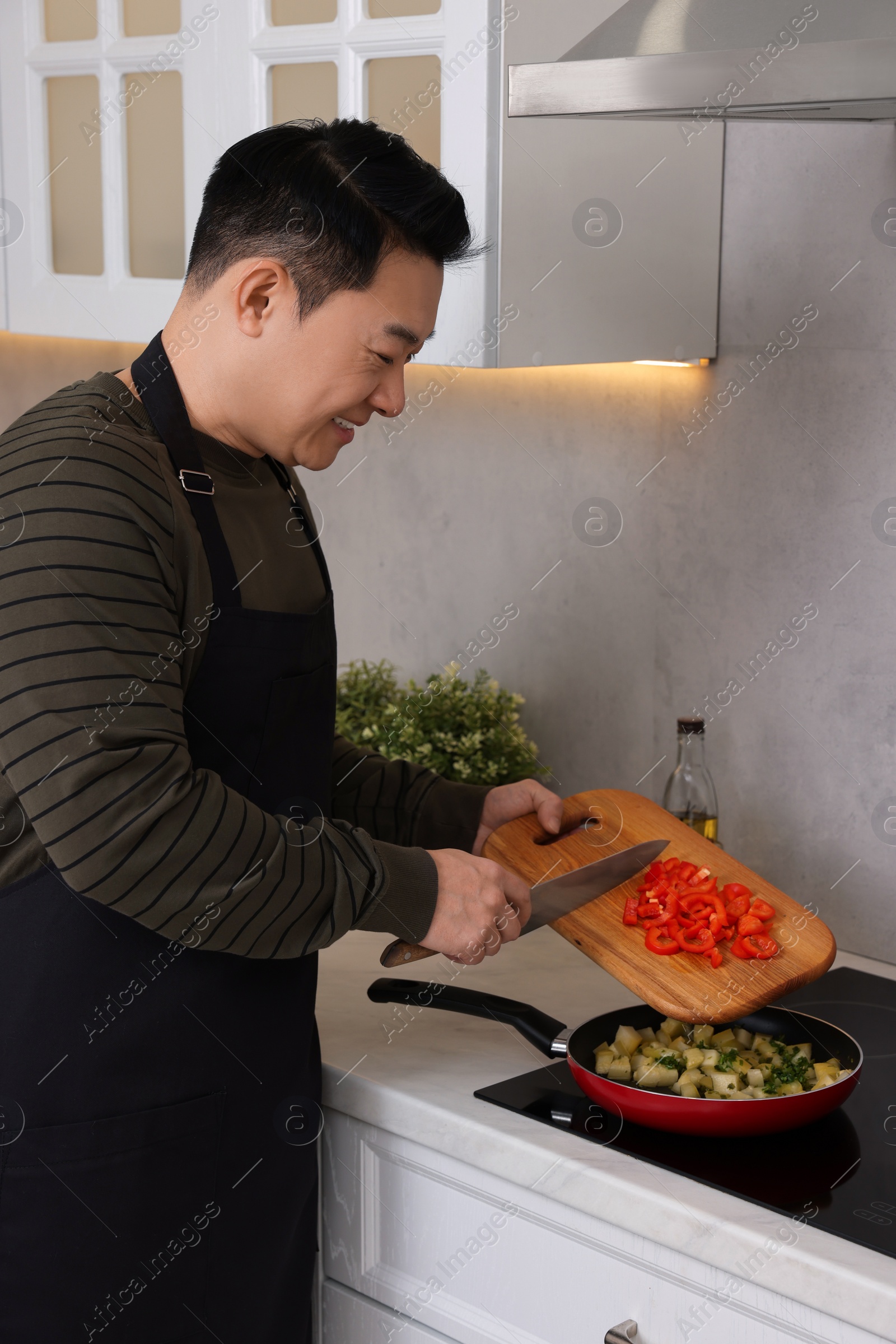 Photo of Cooking process. Man adding cut bell pepper into frying pan in kitchen