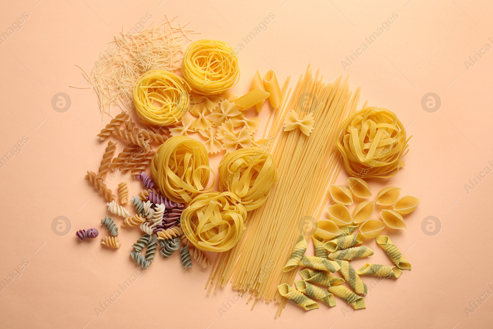 Photo of Different types of pasta on light orange background, flat lay