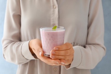 Photo of Woman holding fig smoothie with mint on light blue background, closeup