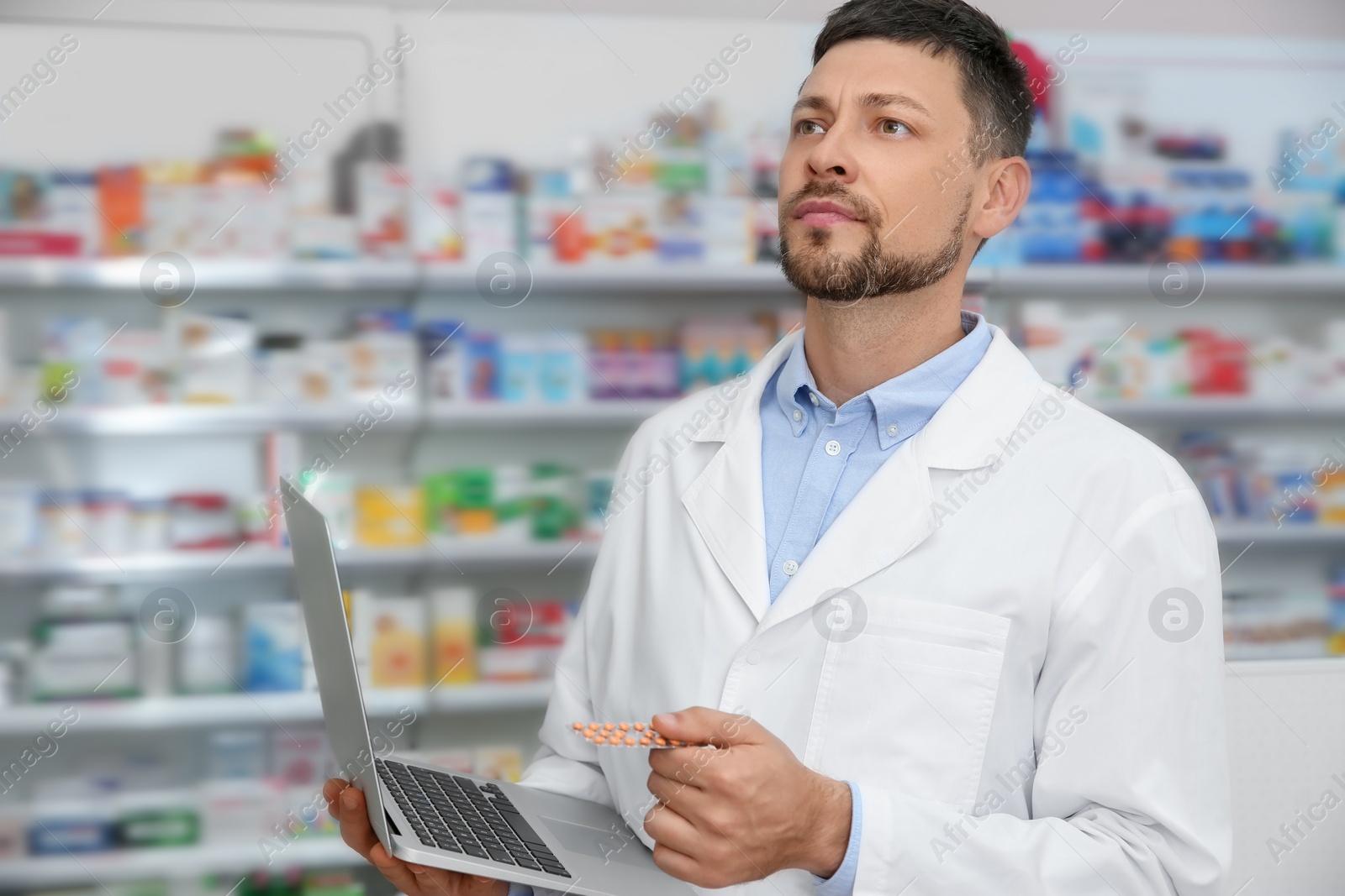 Photo of Concentrated pharmacist with laptop in modern drugstore