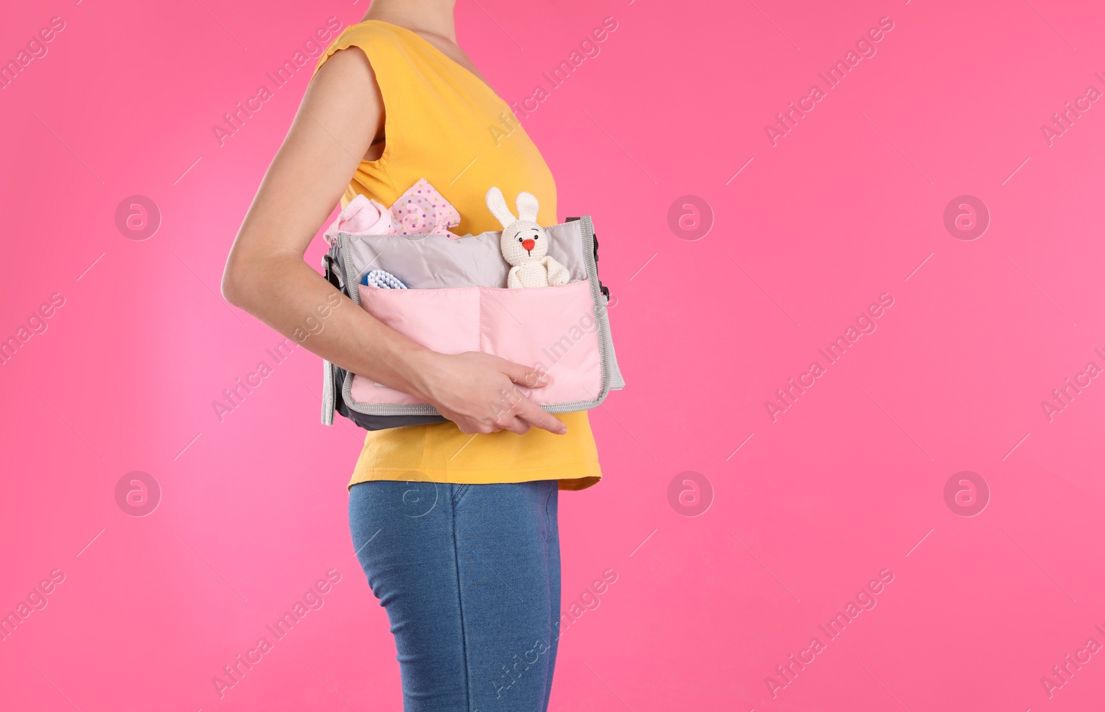 Photo of Woman holding maternity bag with baby accessories on color background, closeup. Space for text