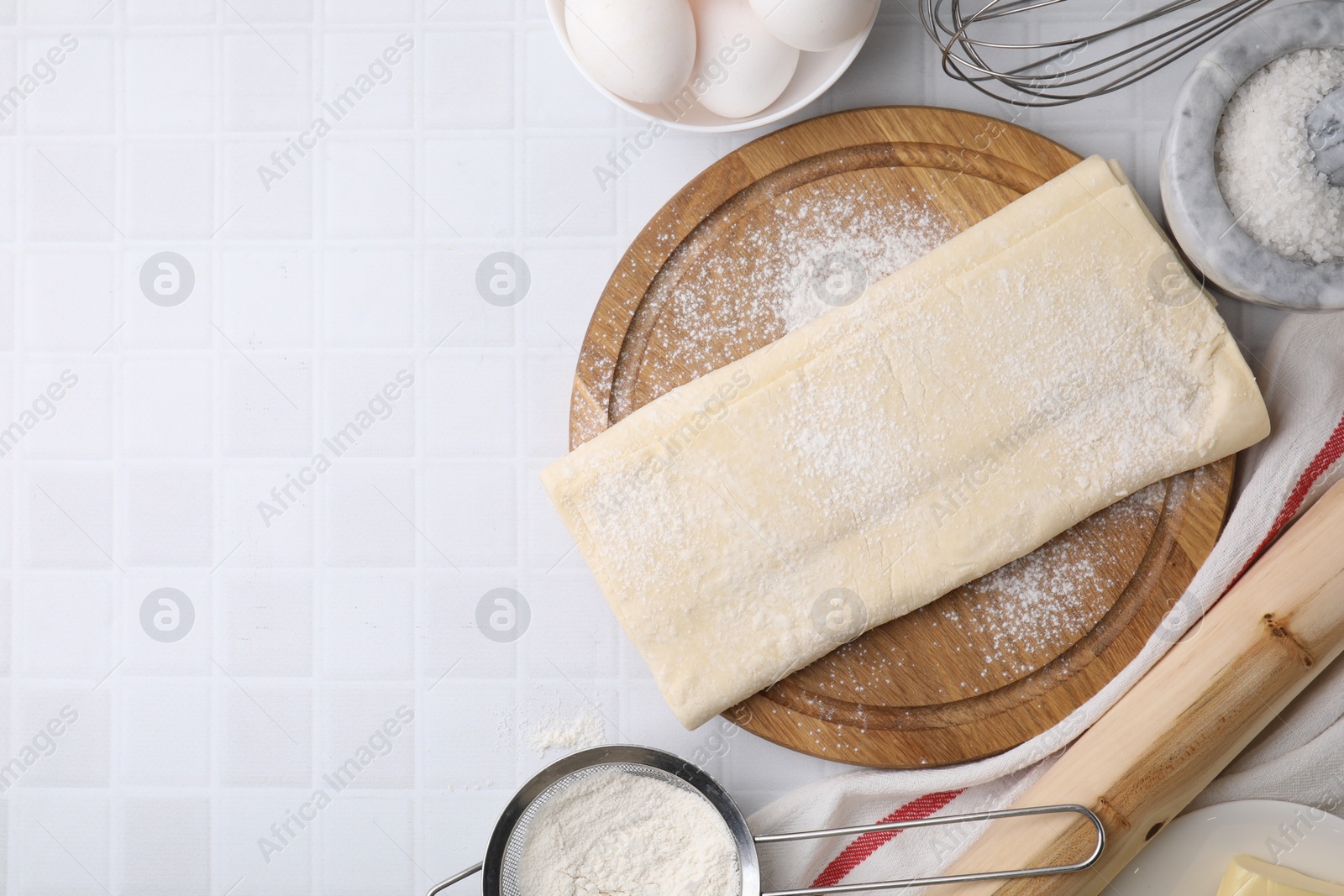 Photo of Raw puff pastry dough and ingredients on white tiled table, flat lay. Space for text