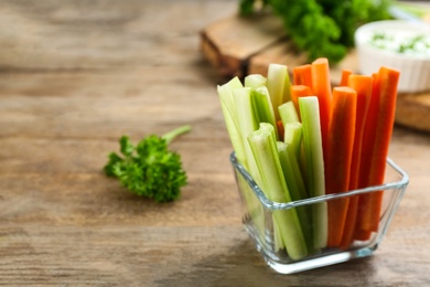 Photo of Celery and carrot sticks in glass bowl on wooden table. Space for text