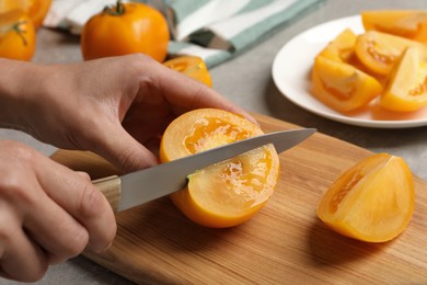 Photo of Woman cutting fresh ripe yellow tomato at light grey table, closeup