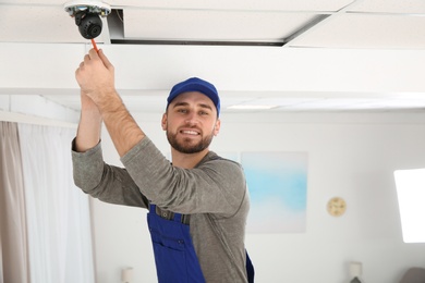 Photo of Electrician with screwdriver repairing CCTV camera indoors. Space for text