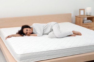 Photo of Happy young African American woman on bed with comfortable mattress at home