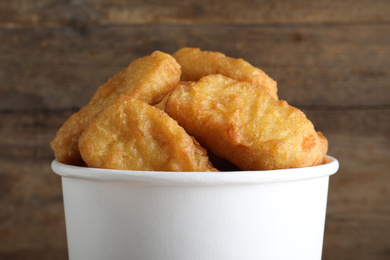 Photo of Bucket with tasty chicken nuggets on wooden background, closeup