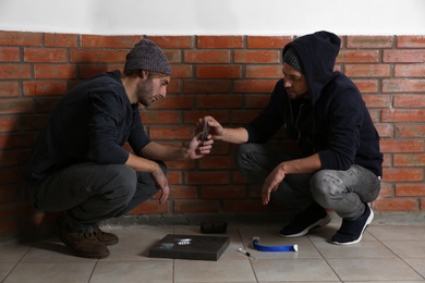 Photo of Young addicted men with drugs near brick wall